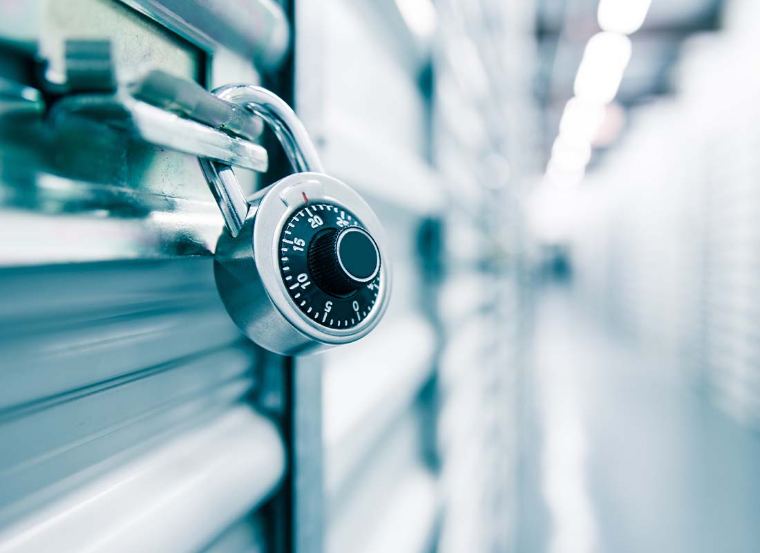 Self Storage Facility Insurance - Close-up Focus On a Combination Lock on a Self Storage Door With the Background of Rows of Storage Facility Doors Blurred