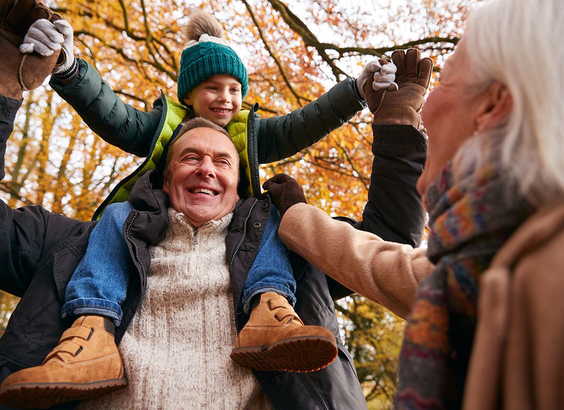 Employee Benefits - Portrait of Cheerful Grandparents Playing with Their Grandson Outside in the Park on a Chilly Fall Day