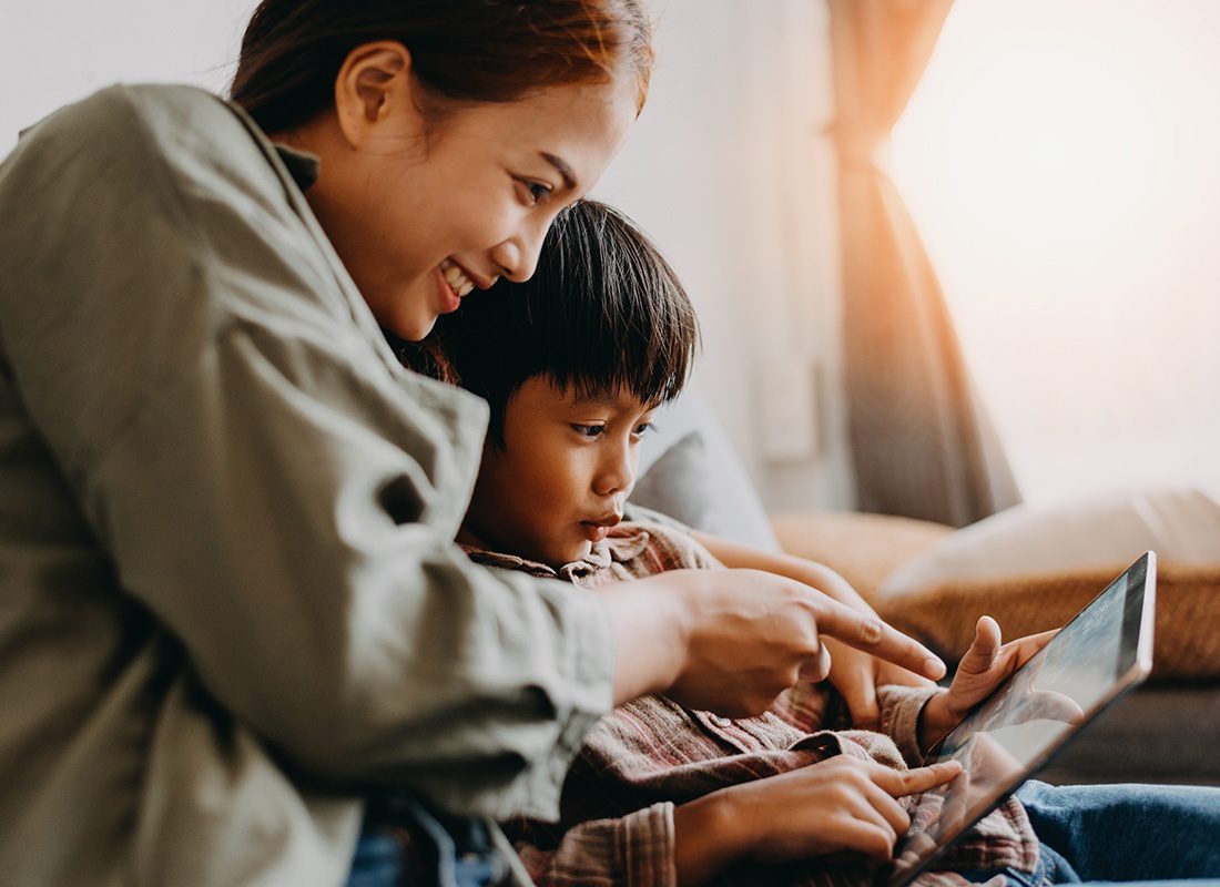 Read Our Reviews - Closeup Portrait of a Cheerful Young Mother Sitting in the Living Room with Her Son as They Use a Tablet Together